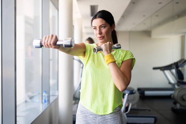 Attraktive Frau trainiert mit Kurzhanteln im Fitnessstudio. - Foto, Bild