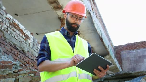 Strojní stavitel v helmě používá tablet, stavební demolici a pohled na stavební projekt - Záběry, video