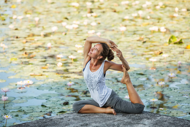 Woman practices yoga on a lake with lotus water lilies - Photo, Image