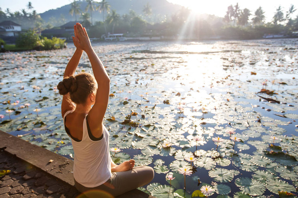 Woman practices yoga on a lake with lotus water lilies - Fotó, kép
