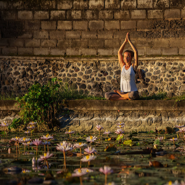 Woman practices yoga on a lake with lotus water lilies - Valokuva, kuva