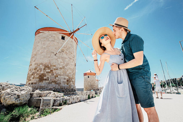 Un par de turistas felices viajan en la ciudad de Rodas frente a los famosos molinos de viento. Grecia concepto de vacaciones
 - Foto, Imagen