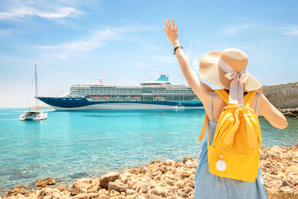 Happy woman tourist with backpack on a coastline, looking at the big cruise liner ship. Purchasing of tour and summer vacation concept - Φωτογραφία, εικόνα