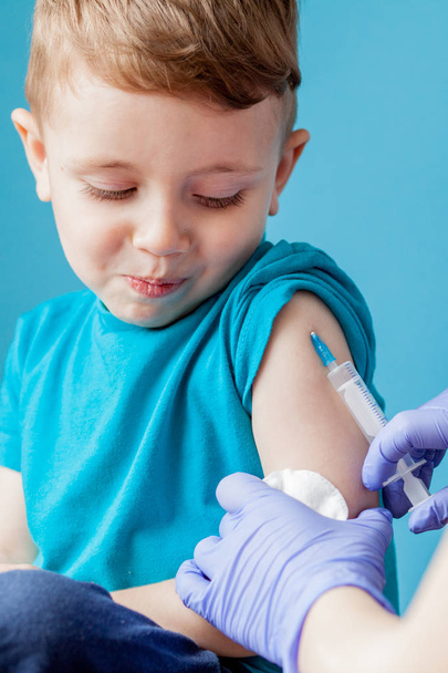 Vaccination concept. Female doctor vaccinating cute little boy on blue background, closeup - Photo, image