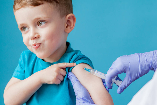 Vaccination concept. Female doctor vaccinating cute little boy on blue background, closeup - Φωτογραφία, εικόνα