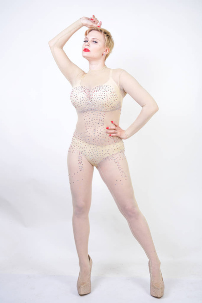 sexy curvy girl in beige lingerie and transparent overalls for whole body in rhinestones posing on white background in the Studio. fashionable young woman with short hair in erotic dance costume. - Photo, Image