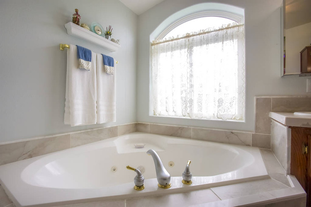 Bathtub with with gold and silver faucet beside an arched window with curtain - Photo, Image