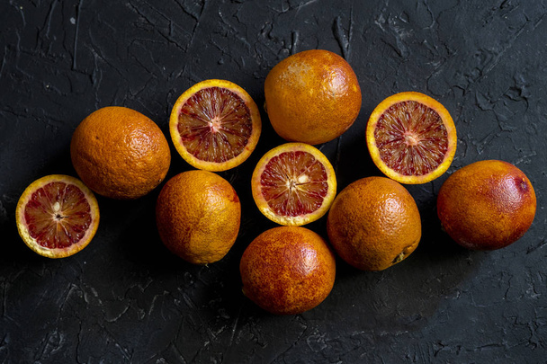 плоская укладка красных нарезанных экзотических апельсинов, темная пища на черных поверхностях - Фото, изображение