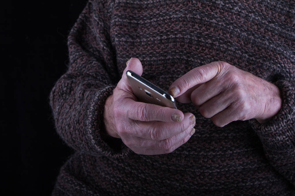 Nahaufnahme der schmerzenden Hände eines sehr alten Mannes bei der Arbeit mit einem Smartphone vor dunklem Hintergrund, selektiver Fokus - Foto, Bild