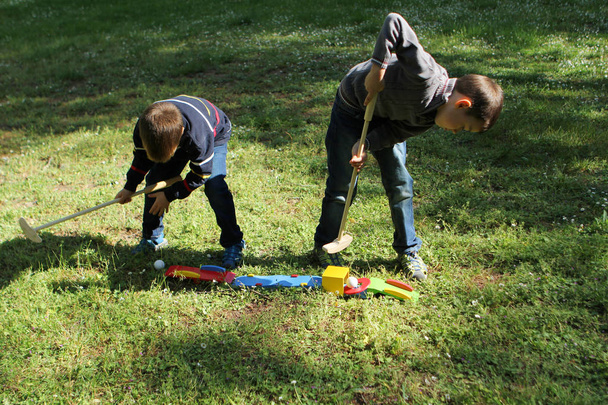 two preschool boys playing wooden mini golf on the grass outside, concept of summer outdoor games - Foto, afbeelding