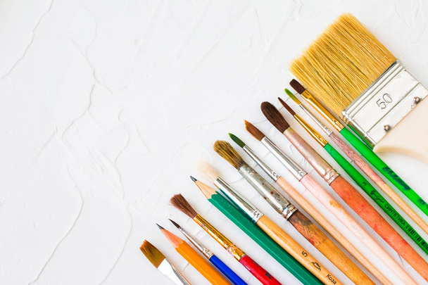 Cepillos y lápices diferentes sobre una superficie blanca. Objeto de arte y educación. Copiar espacio
.  - Foto, Imagen