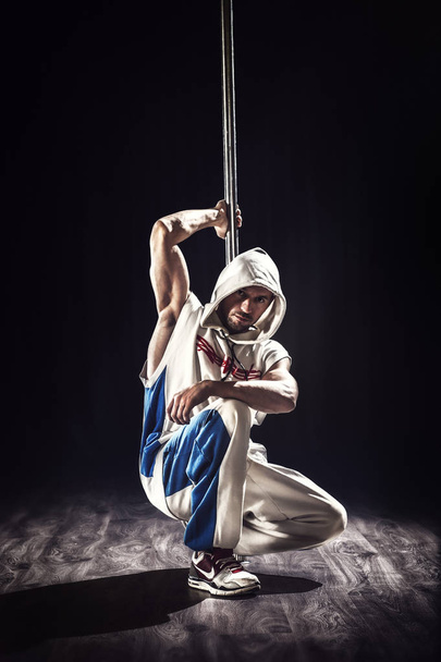 Young hip-hop pole dancer. Athlete, sitting and watching to the camera on the dark background.  - Fotoğraf, Görsel