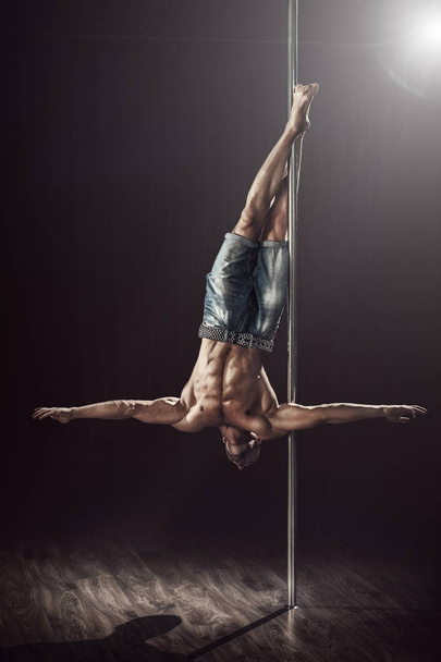 Pole dance male athlete. Strong and muscular guy executes a trick. Pole dancing world champion showing skills.  - Fotó, kép