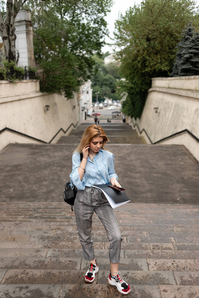 beautiful girl standing on the stone steps holding a notebook and talking on the phone. - Фото, зображення