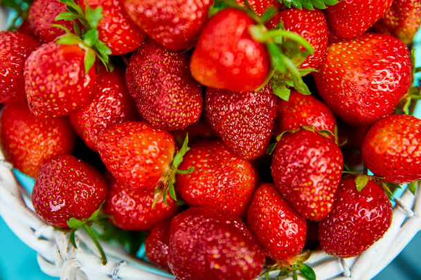 Reife rote Erdbeeren auf blauem Tisch, Erdbeeren im weißen Korb. Frische Erdbeeren. Schöne Erdbeeren. Ernährung. Gesund, vegan. Ansicht von oben. Flache Lage. - Foto, Bild