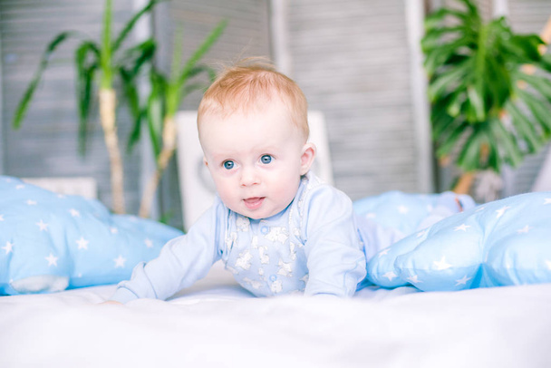 Cute toddler boy on bed at home surrounded by blue pillows - Fotó, kép