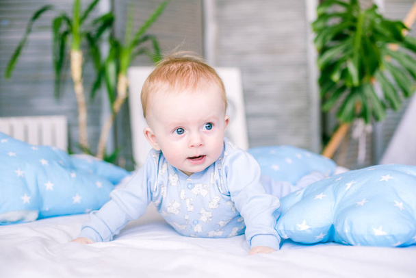 Cute toddler boy on bed at home surrounded by blue pillows - Фото, изображение