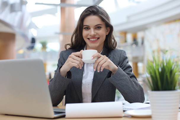 Attractive smiling businesswoman sitting in the office with a cup of coffee. - Valokuva, kuva