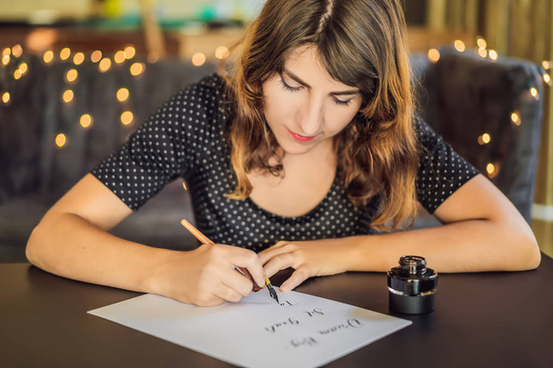 dream big set goals take action. Calligrapher Young Woman writes phrase on white paper. Inscribing ornamental decorated letters. Calligraphy, graphic design, lettering, handwriting, creation concept - Fotó, kép