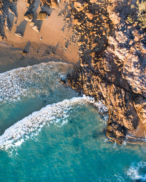 Bela vista aérea de uma fuga de praia com praia agradável, rochas e ondas suaves quentes
 - Foto, Imagem