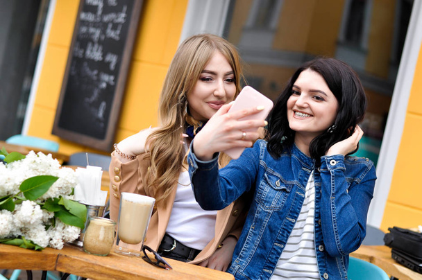 Due ragazze alla moda stanno sorridendo e scattando selfie in un caffè della città
. - Foto, immagini