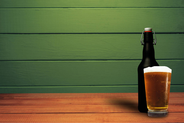 Kieliszek piwa i czarne piwo butelkowe na czerwonym drewnianym stole. Piękne zielone drewno tło. - Zdjęcie, obraz