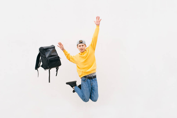 Street young man jumping with a backpack on the background of a white wall. Isolated. Copyspace. Weightlessness. Levitation - Zdjęcie, obraz