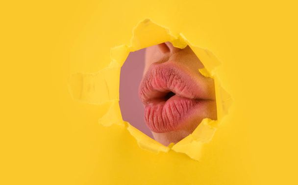 Beautiful plump bright lips of pink color. Mouth peep into the slit of colored paper. Make-up, advertising, facial, boutique, smooth skin, emotions, surprise concept. Woman with pink lips behind hole. - Photo, Image