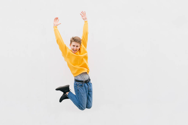 Šťastný muž v příležitostných šatech skáče na pozadí bílé zdi, pouliční portrét. Radostný teenager vyskočil do výšky na bílém pozadí. Copyspace - Fotografie, Obrázek