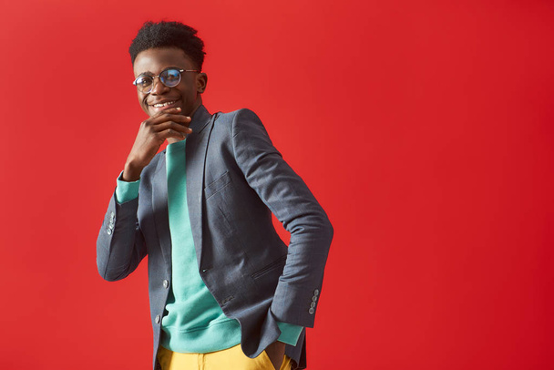 Positive young man in glasses dancing on red background - Fotó, kép