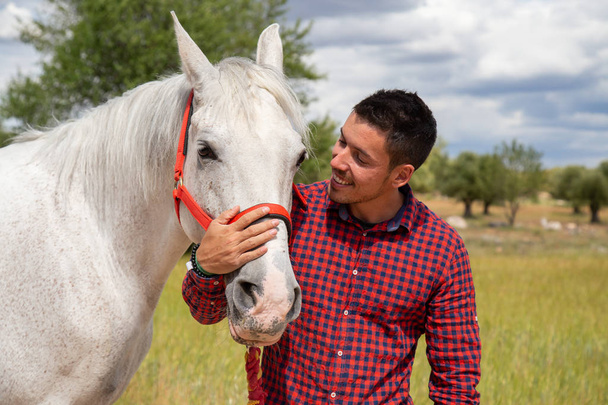 Nuori mies koskettaa valkoista hevosta hellästi
 - Valokuva, kuva