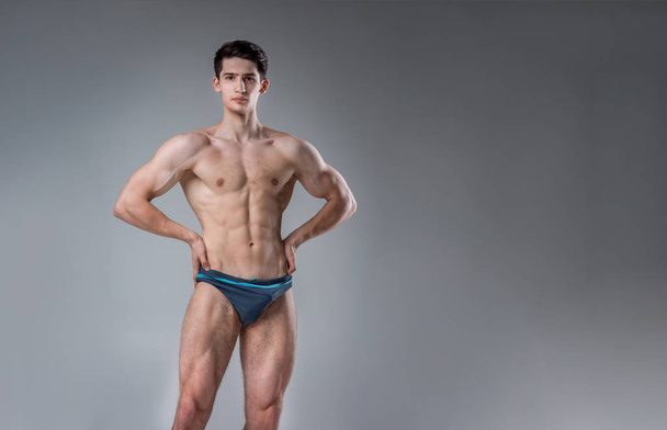 Young male athlete bodybuilder posing. Handsome athletic male power guy. Fitness muscular person. Young athlete showing muscles in the studio. six packs muscles posing shirtless on gray background - Photo, Image