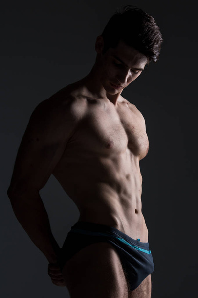 Young male athlete bodybuilder posing. Handsome athletic male power guy. Fitness muscular person. Young athlete showing muscles in the studio. six packs muscles posing shirtless on gray background - Φωτογραφία, εικόνα