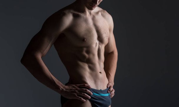 Young male athlete bodybuilder posing. Handsome athletic male power guy. Fitness muscular person. Young athlete showing muscles in the studio. six packs muscles posing shirtless on gray background - 写真・画像