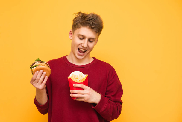Woman eating burger and fries smiling. Beautiful mixed race asian caucasian female model on red background. - Фото, зображення