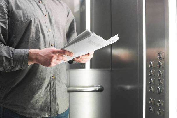 Ділова людина в сірому сорочці тримає папір в руках і навчається в ліфті, обрізаний фото. Руки людини є ліфт і тримати документи, крупним планом. - Фото, зображення