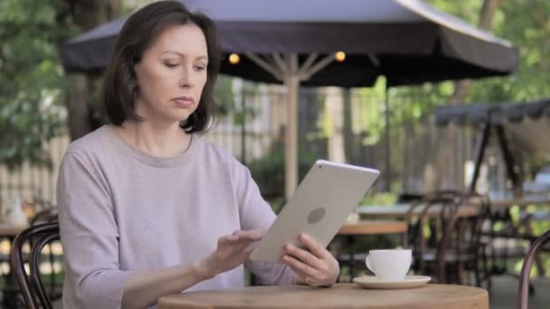 Zdenerwowany stara kobieta reaguje na utratę na tablecie w Outdoor Cafe - Materiał filmowy, wideo