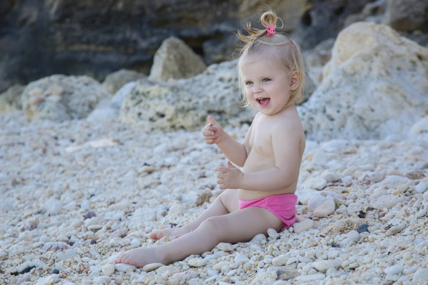 Őszinte portré egy aranyos szőke kislány élvezi a nap a sziklás strandon - Fotó, kép