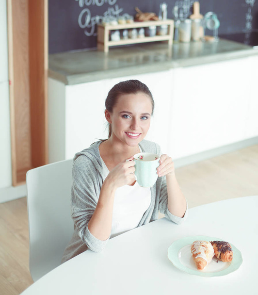 Woman drinking tea with sweet croissant at the kitchen table. - Valokuva, kuva
