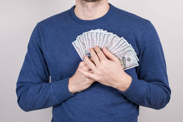 Περικομμένο κοντινό-up στούντιο φωτογραφία του άντρα που ερωτεύεται με χρήματα που κρατούν το στήθος της καρδιάς απομονωμένο γκρι φόντο - Φωτογραφία, εικόνα