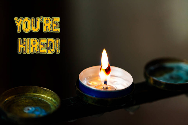 Text sign showing You Re Hired. Conceptual photo Used by huanalysis resources indicate employee that he is got job Abstract burning candle set of three just one shining flame glowing dark. - Photo, Image