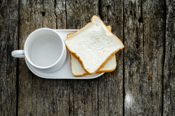 White bread and glass placed on the table in the morning.On the breakfast table there was a glass of coffee and a plate of bread.Breakfast set on wooden floor in the morning. - Foto, Imagem