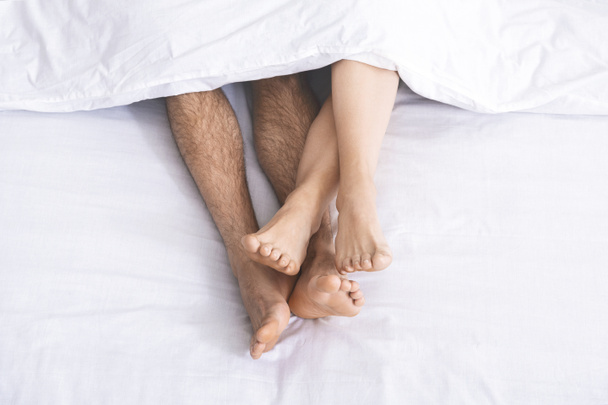 Gambe maschili e femminili sotto il piumone sdraiato sul letto
 - Foto, immagini
