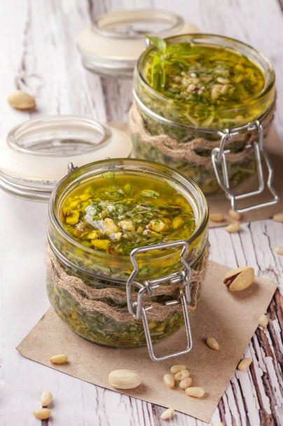 Green pesto sauce. Classic Italian sauce. Preservation in a glass jar. Two jars of sauce decorated in a rustic style.  Close up and vertical orientation.  - Φωτογραφία, εικόνα