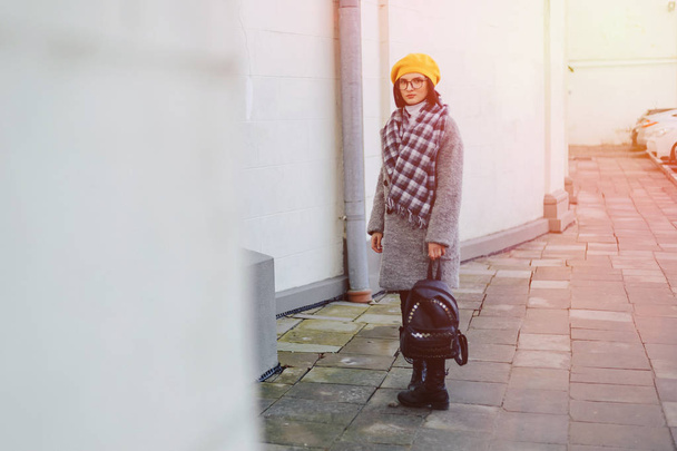 Ελκυστικό νεαρό κορίτσι με γυαλιά στο παλτό και κίτρινο μπερέ ελεύθερο περπάτημα - Φωτογραφία, εικόνα