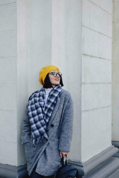 Attractive smiling young girl in glasses in coat and yellow Beret on a simple light background - Photo, Image