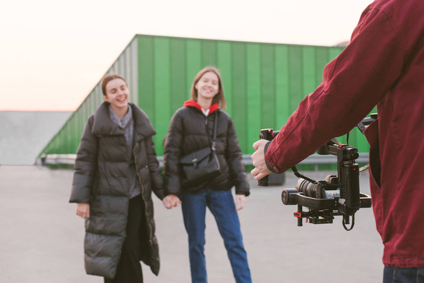 Професійний відеооператор бере на відео двох щасливих дівчат, тримаючи камеру-стабілізатор в руках. Камератор знімає відеоблогери на камеру зі стабілізатором. Створення відеоконтенту. За лаштунками
 - Фото, зображення