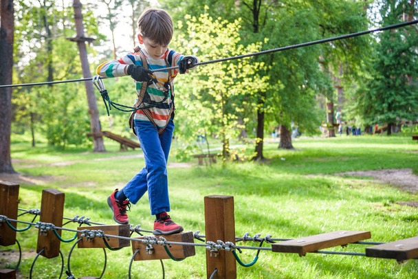 Happy kid playing at adventure park, holding ropes and climbing  - Foto, imagen