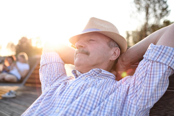 Oude Hispanic man zit op bankje, glimlachend, genieten van de zomer zonnige dag. - Foto, afbeelding