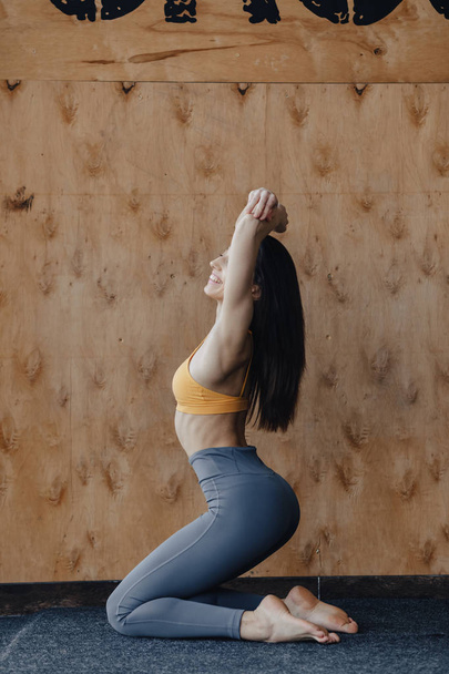 Joven chica atractiva haciendo ejercicios de fitness con yoga en el suelo sobre un fondo de madera
 - Foto, imagen